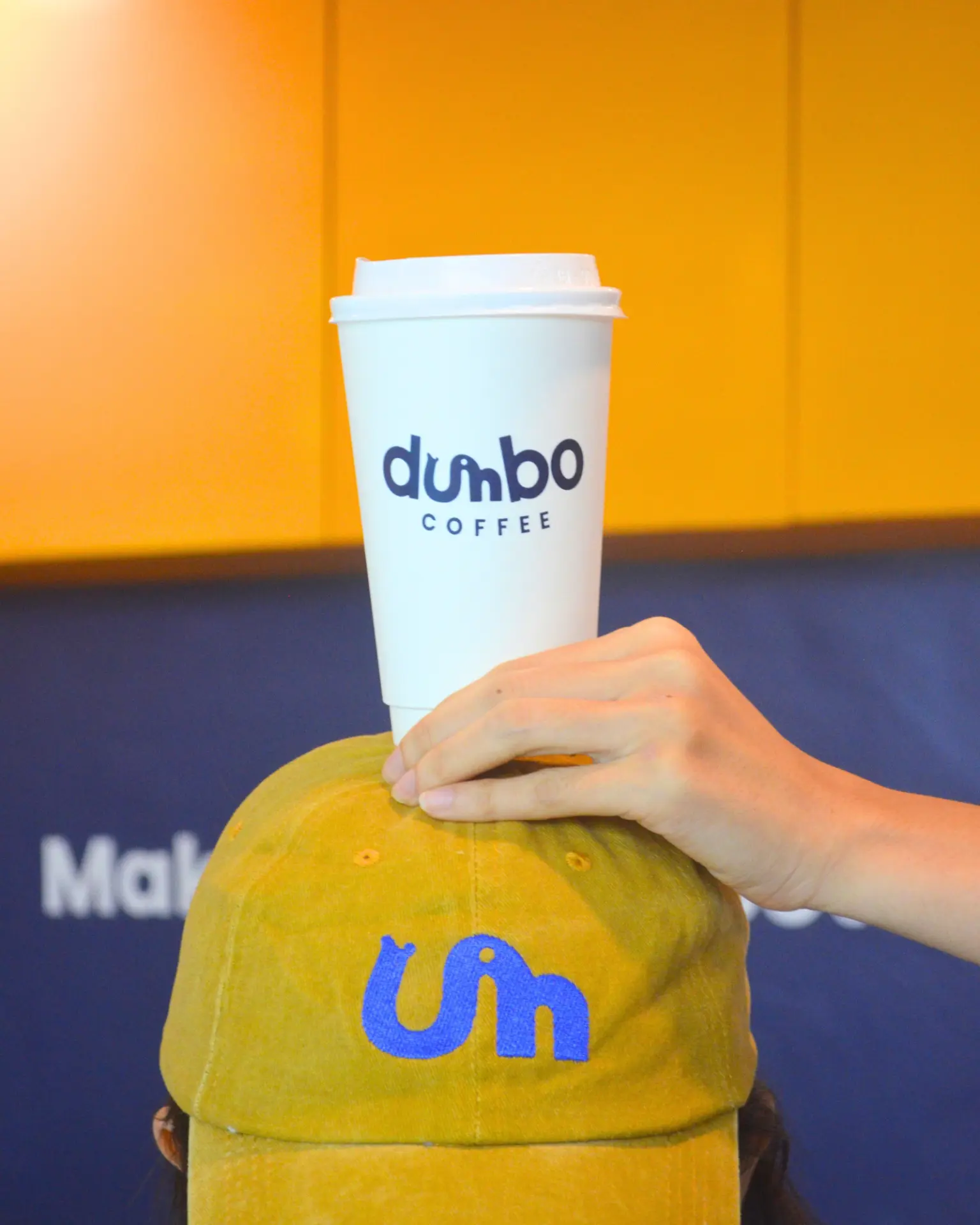 Dumbo Coffee cup balanced above a yellow cap in a bright café setting